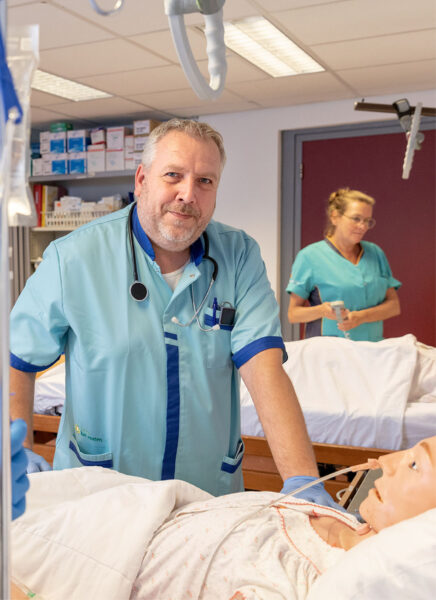 BBL student zorg staat aan het bed en kijkt in de camera
