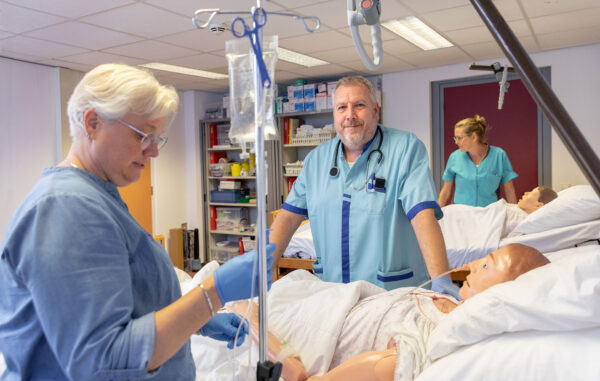 Student volwassenenonderwijs Verpleegkundige in een praktijksetting aan het oefenen bij een bed met patiënt.