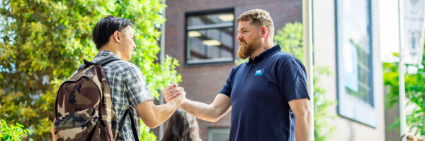 Medewerker Facilitaire dienst van MBO Utrecht begroet student bij de ingang met een enthousiaste groet