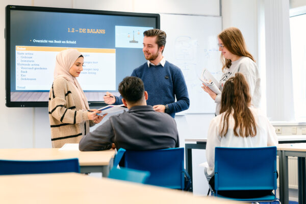 Mbo-studenten Business Services in gesprek met docent in een klaslokaal