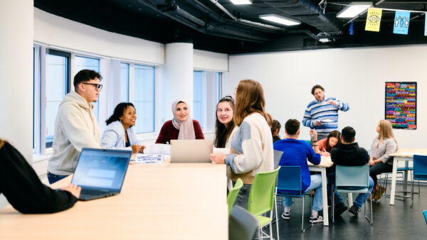Grote groep MBO-studenten Business services en Recht, verzekeringen en HR rond een statafel in gesprek met een docent