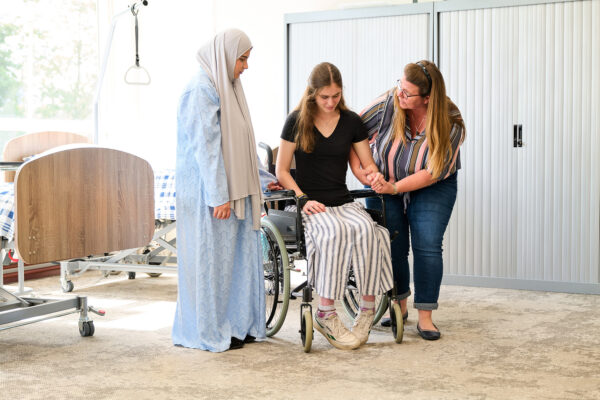 MBO-studenten Maatschappelijke zorg tijdens een praktijkles helpen mede-student uit een rolstoel