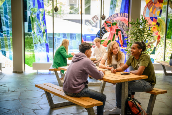 Mbo-studenten chillen samen aan een tafel voor een gekleurd raam