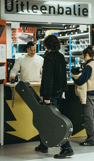 Muziekstudent met gitaar staat bij de uitleenbalie