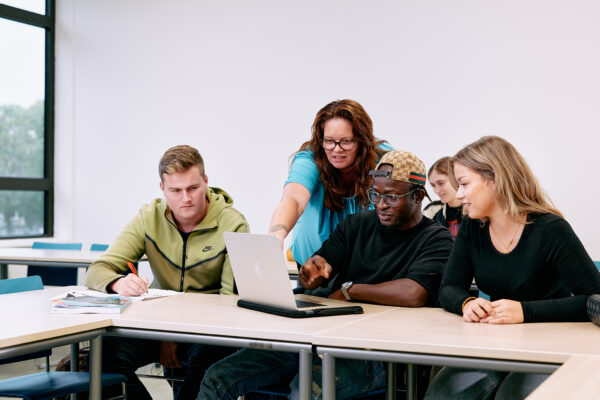 Drie studenten en een docent in een klas. De docent wijst iets aan op de laptop van een student.
